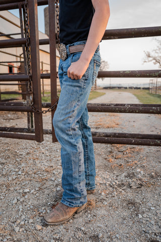 Person wearing blue jeans and a black shirt standing in front of a metal gate.