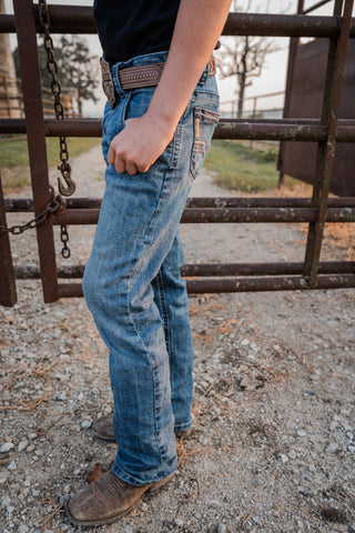 Person wearing blue jeans and a belt standing near a metal gate.
