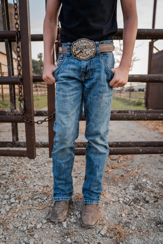 Person wearing blue jeans and a belt with a large buckle standing near a metal gate.
