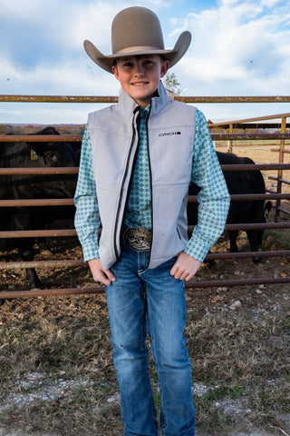 Child in cowboy attire standing in a fenced area with cows in the background