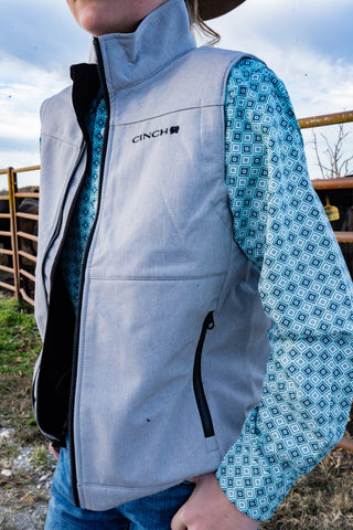 Person wearing a Cinch branded gray vest with a patterned shirt in an outdoor setting.