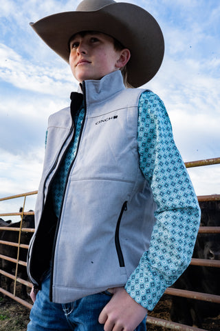 Child wearing a gray vest and cowboy hat with a blue patterned shirt, standing outdoors.