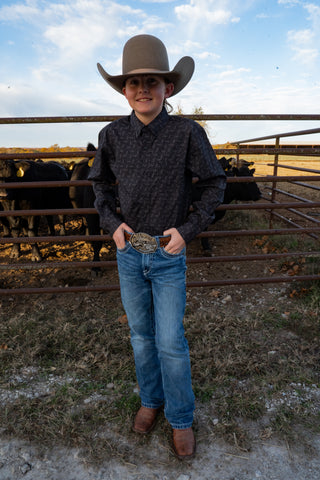 Person wearing a cowboy hat and boots standing in a fenced area with livestock.