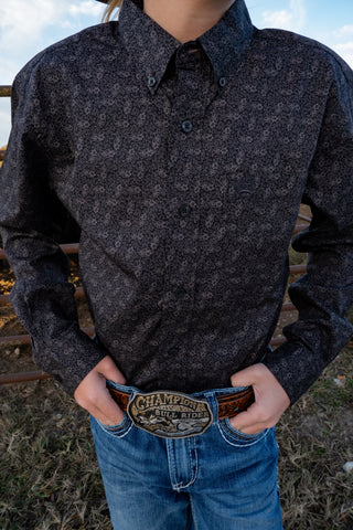 Person wearing a dark patterned shirt and blue jeans with a Champion belt buckle outdoors.