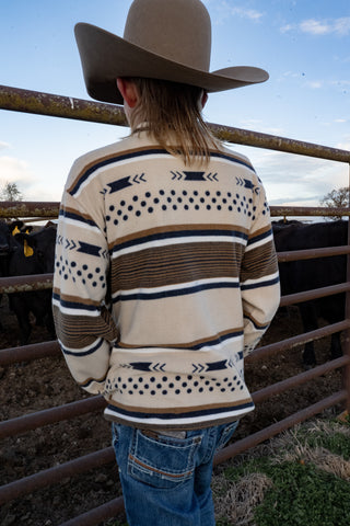 Person wearing a patterned sweater and cowboy hat in a rural setting with livestock.