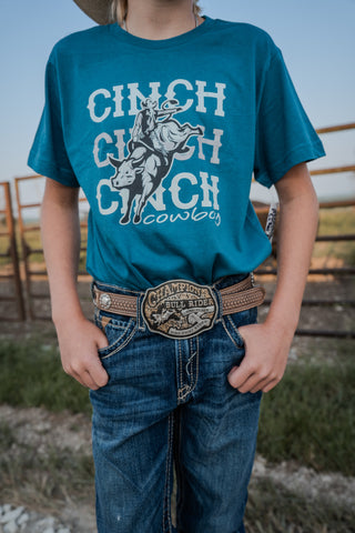 Person wearing a teal t-shirt with 'Cinch' branding and jeans outdoors.