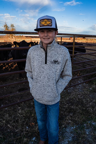 Person wearing a cap and sweater standing in a fenced area with cows in the background