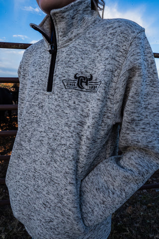 Person wearing a gray pullover with a logo on the chest against a blurred outdoor background