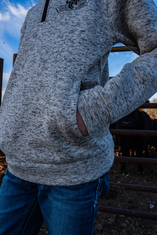 Person wearing a gray hoodie with a logo, standing outdoors with a metal fence and blue sky in the background.