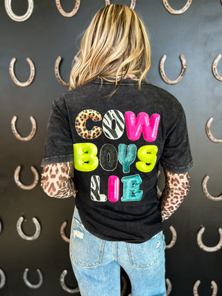 Person wearing a black t-shirt with colorful text and leopard print sleeves, standing against a wall with horseshoe patterns.