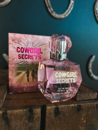 Cowgirl Secrets perfume bottle and packaging on a wooden surface with a dark background
