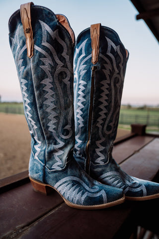 Blue patterned cowboy boots on a wooden surface with a blurred outdoor background
