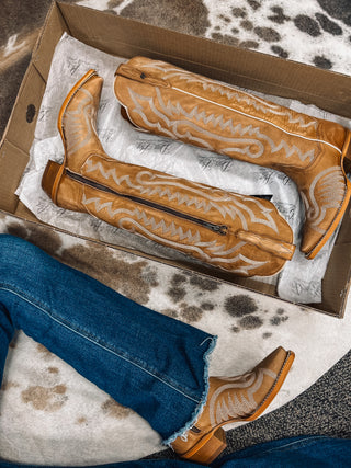 Pair of brown cowboy boots with white patterns in a box on a cowhide rug.