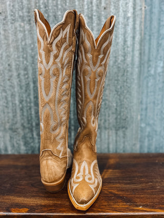 Pair of brown cowboy boots with white embroidery on a wooden surface and textured blue background