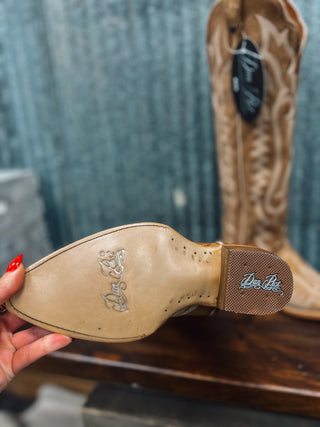 Close-up of a cowboy boot sole with brand logos, held by a hand against a blurred background.