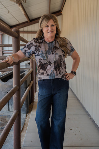 Woman standing on a wooden platform wearing a patterned shirt and jeans.