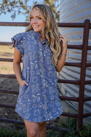 Woman wearing a blue dress with patterns standing in front of a metal fence.
