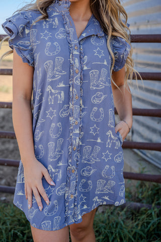 Woman wearing a blue dress with cowboy print against a metal fence background