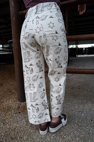 Person wearing cream-colored pants with black patterns of animals and stars, standing on a concrete floor.