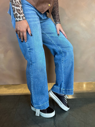 Person wearing blue jeans and black sneakers with a brown background