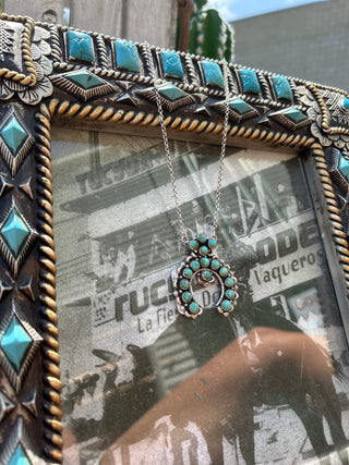 Turquoise and silver necklace displayed in a decorative frame with newspaper background