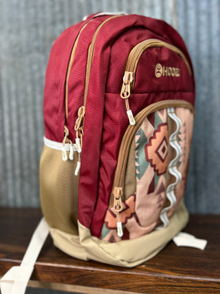 Red and beige backpack with patterned side pocket on a wooden surface