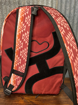 Red bag with geometric pattern and black 'H' logo on a wooden surface