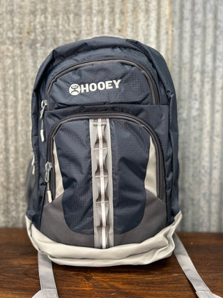 Black backpack with 'Hooey' logo on a wooden surface and metal wall background