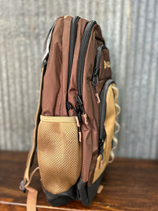 Brown and beige backpack on a wooden surface with a metal wall background