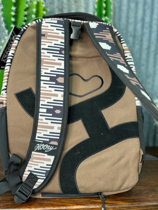 Beige backpack with black and patterned straps on a wooden surface