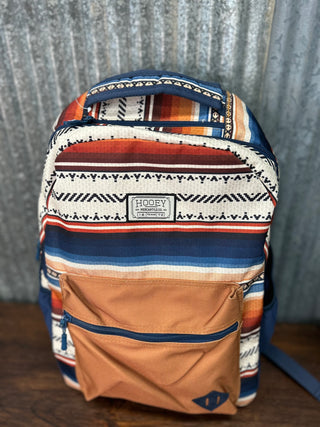 Multicolored patterned backpack with a visible brand logo on a textured surface.