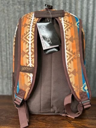 Backpack with patterned straps and visible brand tag on a wooden surface.
