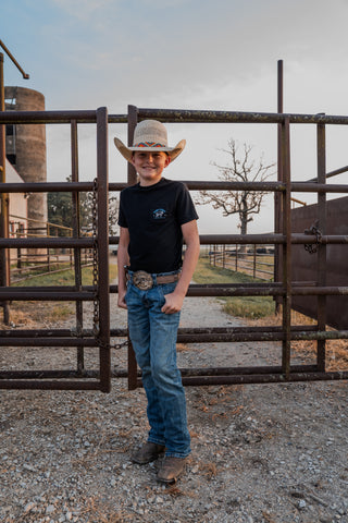 Person wearing a cowboy hat and black shirt standing in front of a metal gate on a farm.