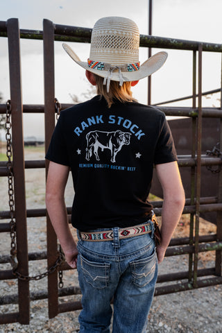 Person wearing a black t-shirt with 'Rank Stock' branding and a cowboy hat, standing in front of a metal gate.