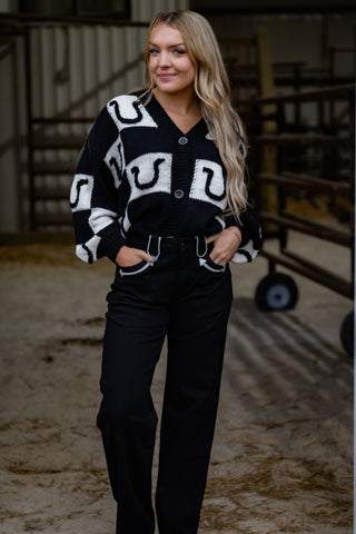 Woman wearing a black cardigan with large white letters in an indoor setting