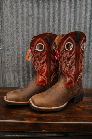 Pair of brown cowboy boots with red and white designs on a wooden surface and metal wall background.