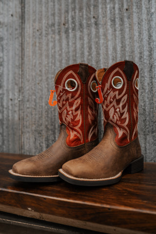 Pair of brown cowboy boots with red and white designs on a wooden surface.