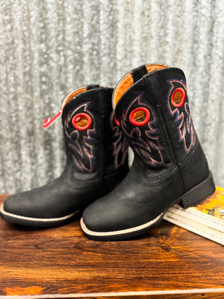 Black cowboy boots with red eyelets on a wooden surface and textured gray background