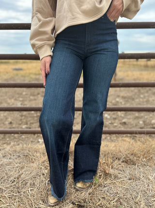 Person wearing blue jeans standing in a field with a metal fence in the background