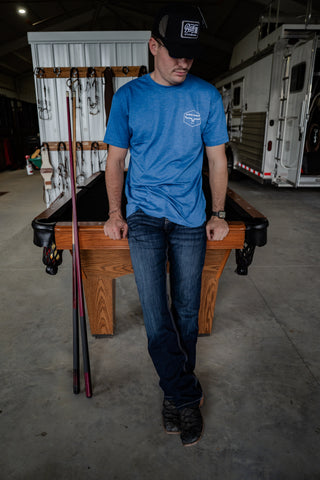Man in a blue shirt standing next to a pool table in an indoor setting