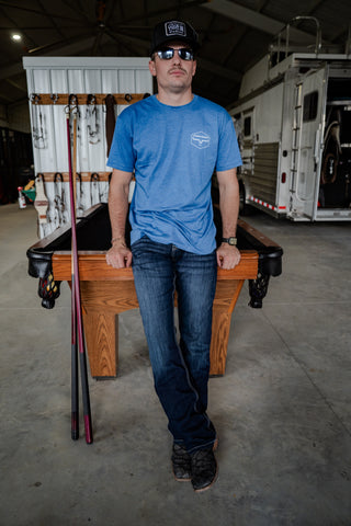 Man in a blue shirt standing next to a pool table in a warehouse setting