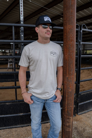 Man wearing a cap and sunglasses, standing in a barn-like setting.