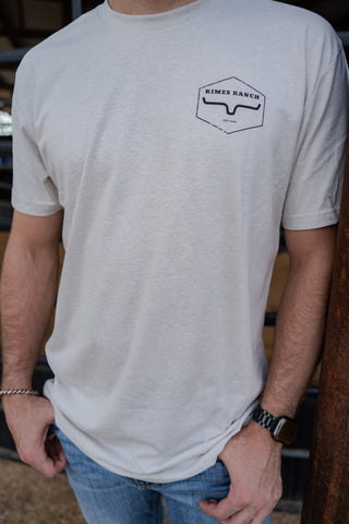 Person wearing a white t-shirt with a logo on the chest, standing indoors.