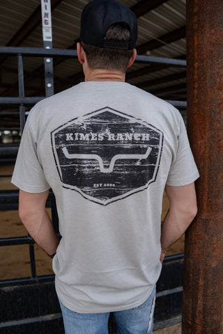 Person wearing a gray t-shirt with 'Kimes Ranch' logo in an indoor setting.