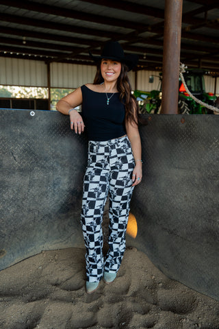 Woman standing in a barn-like setting wearing a black top and checkered pants.