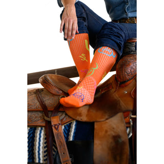 Person wearing orange socks with blue and green designs on a horse saddle