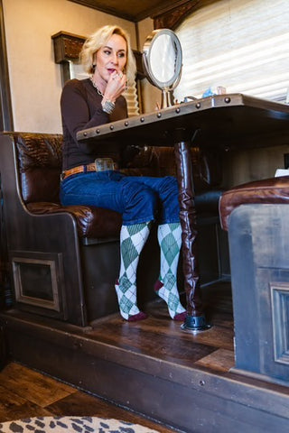 Woman sitting at a table in a rustic setting wearing argyle socks.
