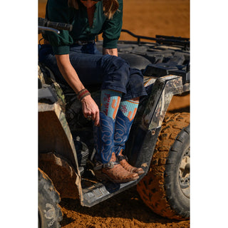 Person wearing blue jeans and patterned socks sitting on a four-wheeler in a desert setting