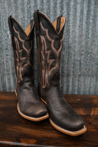 Pair of black cowboy boots with intricate designs on a wooden surface and textured gray background
