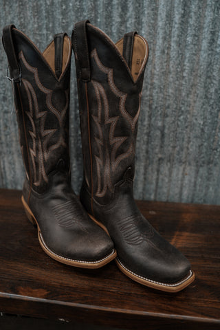 Pair of black cowboy boots on a wooden surface with a textured blue background